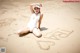 A woman in a white bathing suit sitting on a sandy beach.