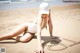 A woman in a white bathing suit and hat laying on the beach.