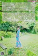 A woman in a blue kimono standing in a garden.