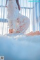 A woman in a white lace robe sitting on a bed.