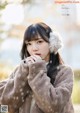 A woman wearing a brown coat and ear muffs in the snow.