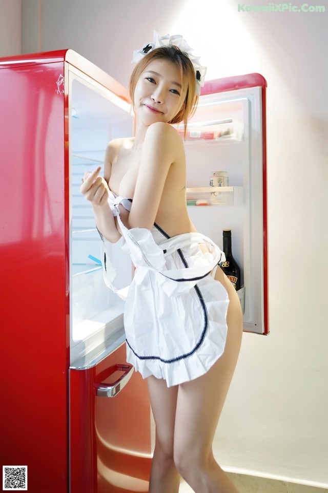 A woman in a maid outfit standing in front of a refrigerator.