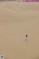 A woman in a blue dress walking across a sand dune.