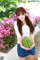 A young woman holding a watermelon in front of flowers.