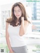 A woman in a white tank top and gray skirt posing by a window.