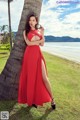 A woman in a red dress leaning against a palm tree.