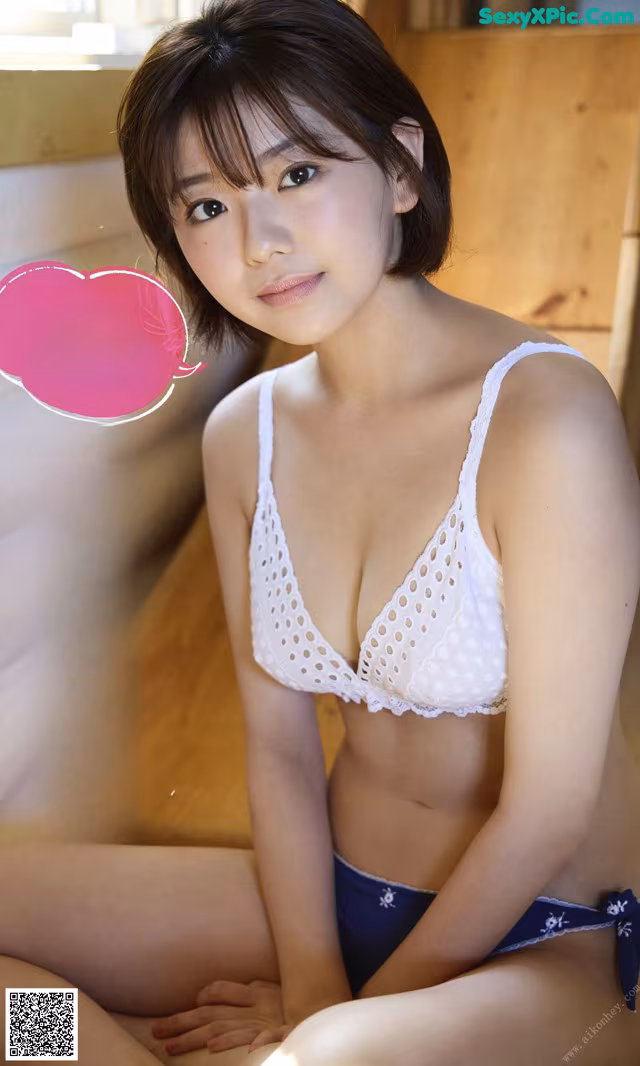 A woman in a white bra and blue panties sitting on a bed.