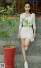 A woman in a white top and skirt posing next to a potted plant.