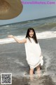 A woman in a white dress and a straw hat on the beach.