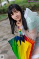 A woman in a white dress holding a rainbow colored umbrella.