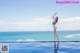 A woman in a green bikini standing on the edge of a swimming pool.