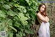 A woman in a white dress standing in front of a bush.